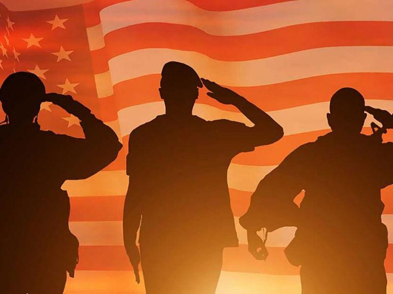 Silhouettes of military people saluting in front of a sunset with the American Flag overlaid on the background
